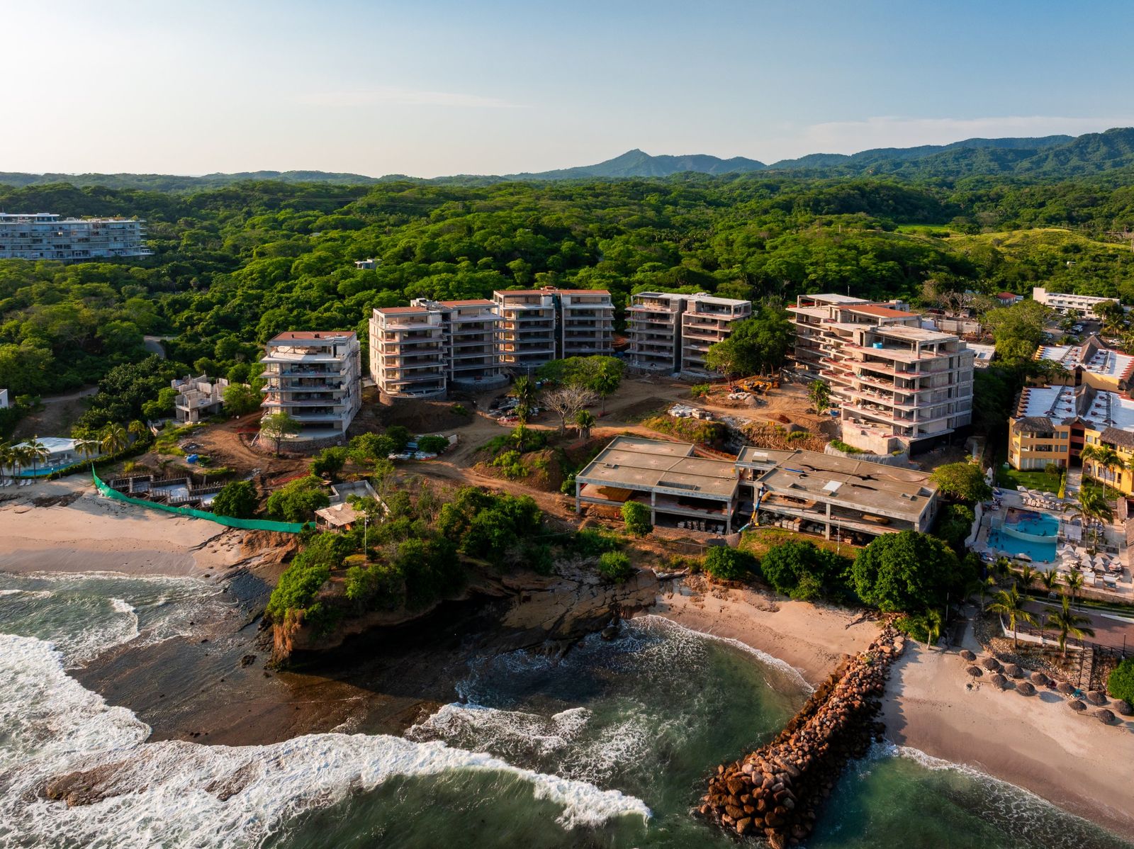 Vista aérea de Maena en construcción frente al mar en Punta Mita, Riviera Nayarit, con la selva y la sierra al fondo